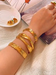 Detailed close-up of gold-plated leaf and feather bangles with a ring on a model hand