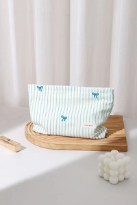 Close-up of blue striped makeup bag with small bow patterns on a wooden tray