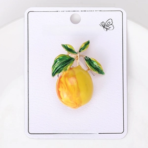 Close-up of a lemon-shaped brooch with yellow enamel finish and green leaves on display card