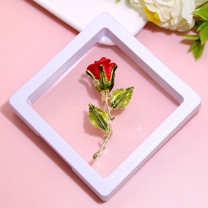 Elegant red rose brooch with green leaves in a white gift box on pink background