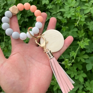 Silicone bead keychain bracelet with wooden hexagon bead and pink tassel held by a hand