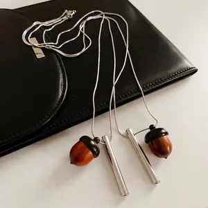 Modern wooden acorn pendant necklace with silver snake chain on black leather bag