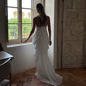 Elegant backless white maxi dress with V-neck and draped skirt by a window