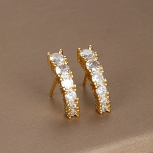 Detailed view of curved gold stud earrings with round clear gemstones in claw settings