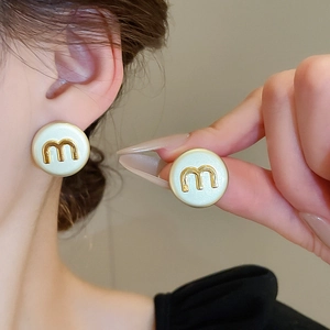 Detail of round cream enamel stud earring with gold metal letter m on woman's ear