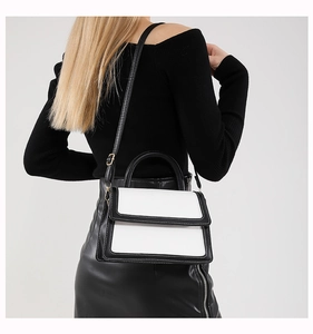 Model wearing a black and white contrast leather handbag with a top handle and shoulder strap