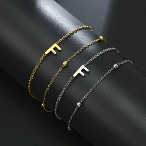 Detail of double-layer gold and silver chains featuring letter F and metallic beads