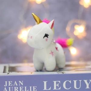 Detail of plush unicorn keychain with golden horn and pink mane on a purple book