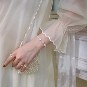 Elegant baroque pearl bracelet and matching rings styled with a luxury pearl handbag