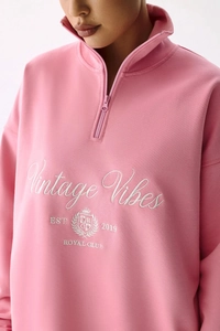 Détail de la broderie blanche sur le sweat rose à demi-zip montrant la texture du tissu