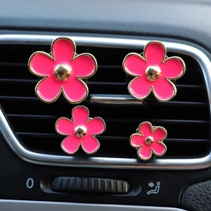 Detailed view of four pink daisy car air vent clips installed on dashboard grille