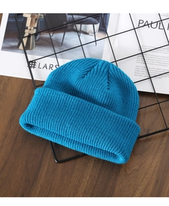 Detail of teal knitted beanie showing thick texture and wool fibers on a wooden surface