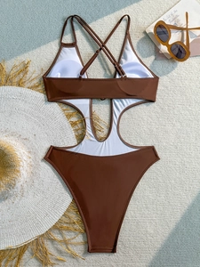 Detailed flat lay of brown cutout one-piece swimsuit with cross straps and summer props