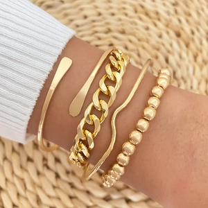 Detail of four-piece gold bracelet set featuring Cuban chain, beads, and wave cuffs on wrist
