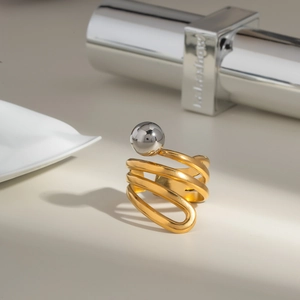 Dettaglio di un anello a spirale dorato con una sfera in argento in stile industrial minimal