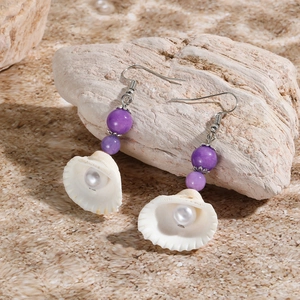 Macro detail of ocean-style earrings with purple beads and shells on a sandy rock beach
