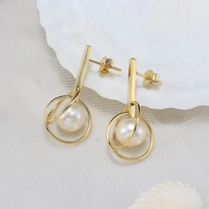 Elegant gold drop earrings with round white pearls on a soft lace and shell background