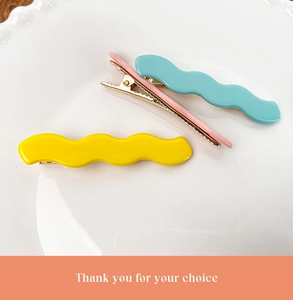 Close-up of wavy macaron hair clips in pink, yellow and blue on a white ceramic plate