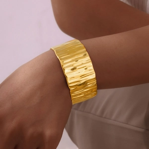 Macro shot of gold-plated wide cuff bracelet with wavy textured surface on wrist