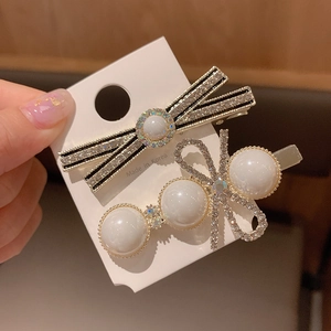 Detail of two gold metal hair clips with pearls and rhinestones on a white card
