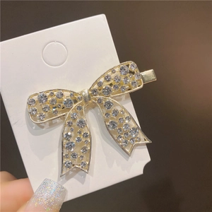 Detailed view of a gold bow hair clip adorned with sparkling crystals on a white card