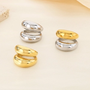 Polished chunky teardrop rings in gold and silver finish on neutral stone background