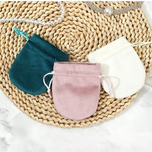 Thick velvet drawstring jewelry pouches in green, pink, and beige on a marble surface