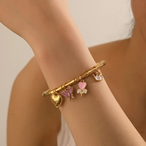 Close-up of a gold bamboo-style bangle with colorful butterfly and heart charms on a wrist
