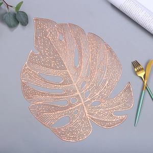 Hollowed out gold Monstera leaf placemat on grey table with elegant cutlery and greenery