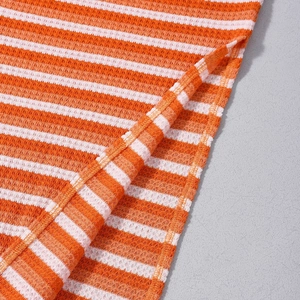 Detailed close-up of orange and white striped waffle knit fabric with side slit stitching