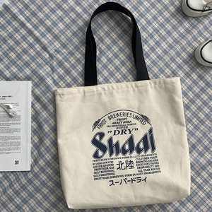 Detailed top view of beige canvas tote bag with artistic beer illustration on blue plaid cloth