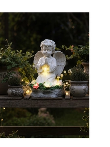 Detalle de estatua de ángel solar de resina con cruz brillante y base floral en el jardín