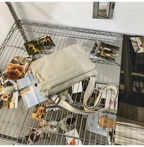 Detail view of a beige nylon crossbody bag with wide adjustable strap and zipper pocket