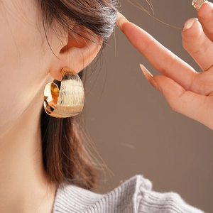 Close-up of gold chunky C-shaped hoop earring with brushed metal texture on female model