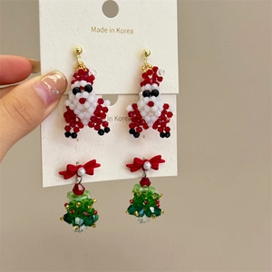 Macro detail of handmade beaded Christmas tree and Santa Claus earrings set with red bows