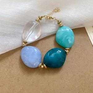 Detail view of acrylic oval beaded bracelet with blue swirl textures and gold links