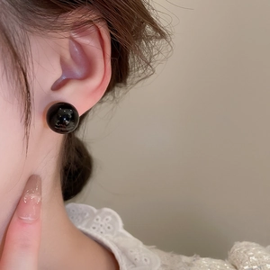 Close-up of minimalist black resin stud earrings worn on the ear for a luxury look