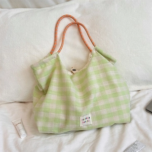 Detail of light green plaid tote bag featuring orange rope handles and woven brand label