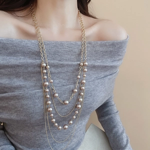 Close-up of a layered gold-tone chain necklace featuring champagne faux pearls on a model