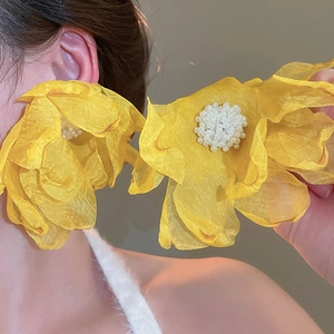 Macro detail of oversized yellow petal mesh earrings with white faux pearl core