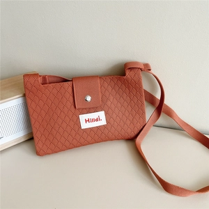 Detail of terracotta knitted crossbody bag with textured diamond pattern and logo label