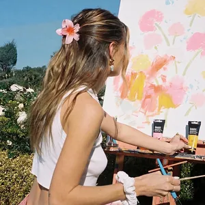 Pink matte lily flower hair claw clip worn by a model painting in an outdoor garden