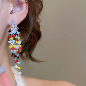 Close-up of dangling tassel earrings with colorful heart beads and teardrop zircon crystal
