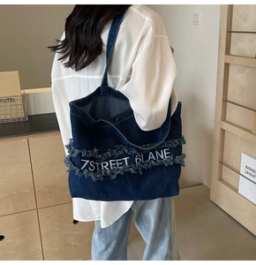 Détail d'un grand sac cabas en denim bleu avec broderie 7STREET blanche et bords effilochés