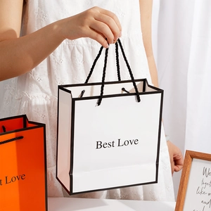 Elegant floral gift bags in white and orange with black woven handles for birthdays