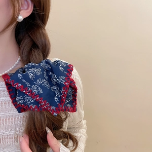 Detail of blue floral oversized bow scrunchie with red stitching on brown wavy hair