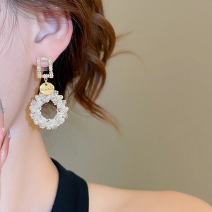 Close-up of golden earring with square zircon stud and woven pearl ring on model