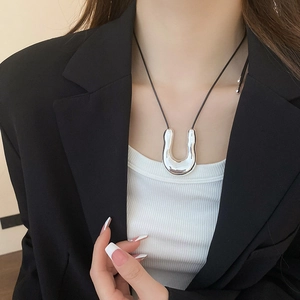 Close-up of a silver U-shaped metal pendant necklace on a model wearing a black blazer