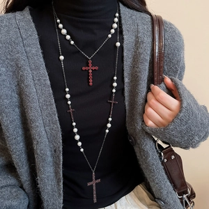 Detail der mehrlagigen Perlenkette mit rotem Strass-Kreuzanhänger auf schwarzem Pullover