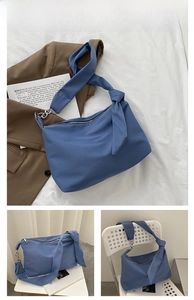 Detail of blue crescent crossbody bag featuring knotted shoulder strap and metal hardware